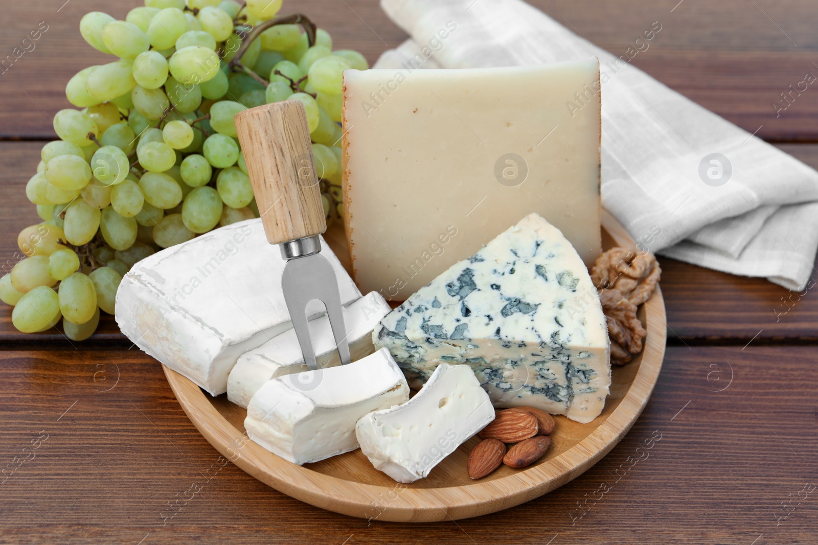 Photo of Different types of delicious cheeses, nuts and grapes on wooden table