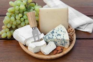 Photo of Different types of delicious cheeses, nuts and grapes on wooden table