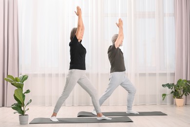 Photo of Senior couple practicing yoga on mats at home