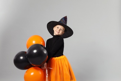 Cute little girl with balloons wearing Halloween costume on grey background, space for text