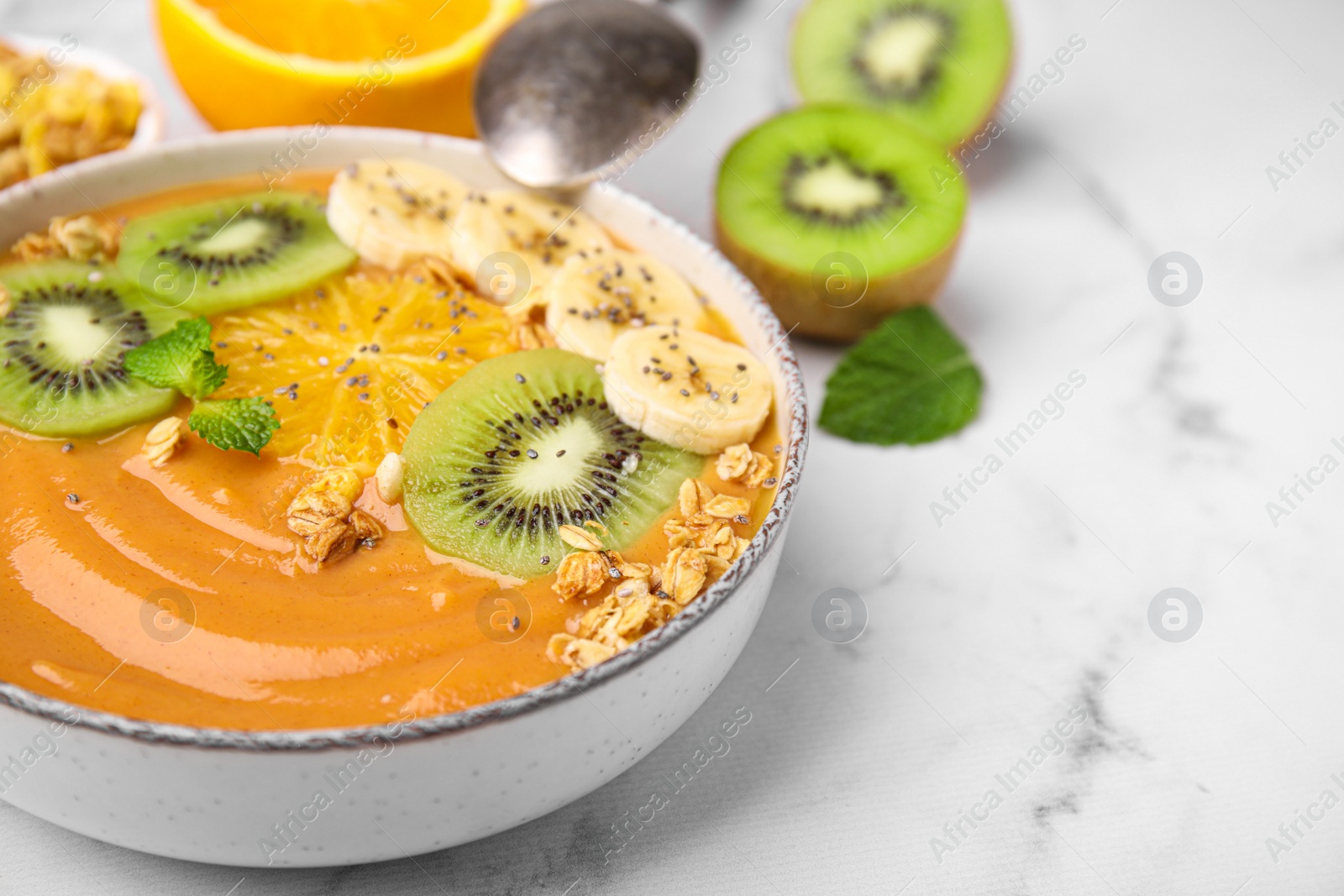 Photo of Bowl of delicious fruit smoothie with fresh banana, kiwi slices and granola served on white marble table, closeup. Space for text