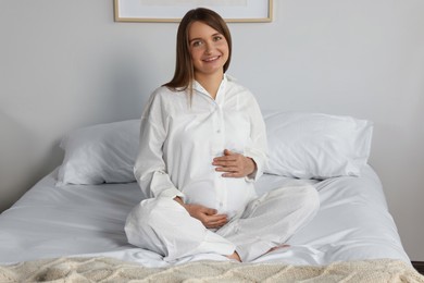 Photo of Happy young pregnant woman in pajamas on bed at home