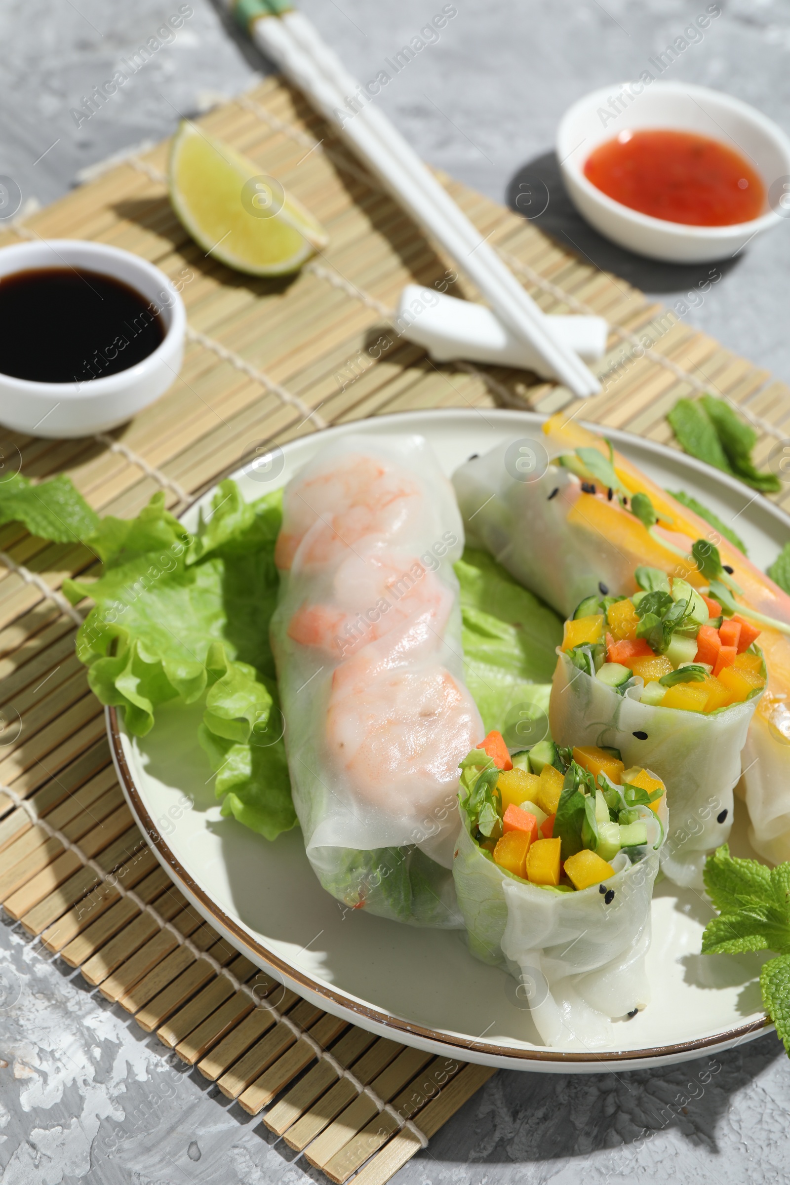 Photo of Tasty spring rolls and sauces on grey textured table, closeup