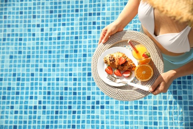 Young woman with delicious breakfast on tray in swimming pool, top view. Space for text