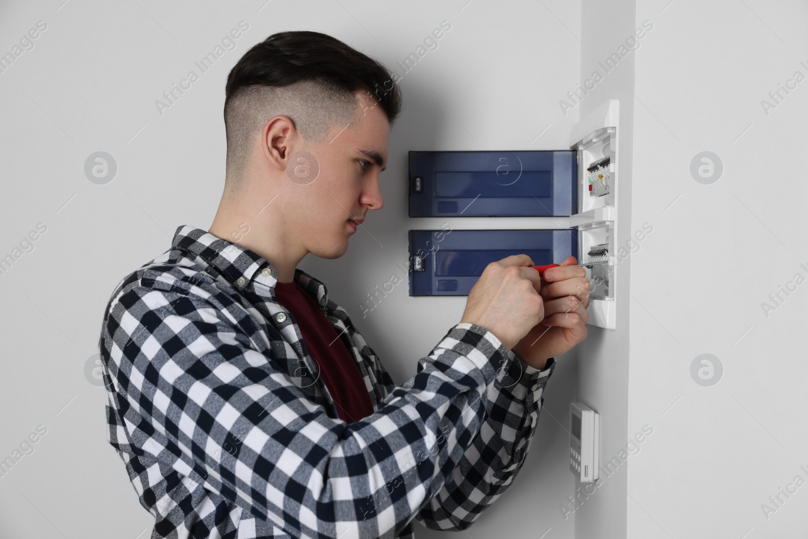 Photo of Young handyman with screwdriver repairing electrical panel board indoors