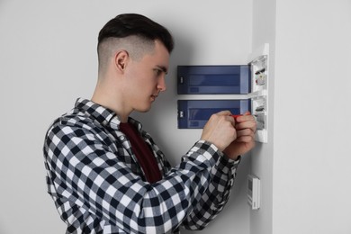 Young handyman with screwdriver repairing electrical panel board indoors