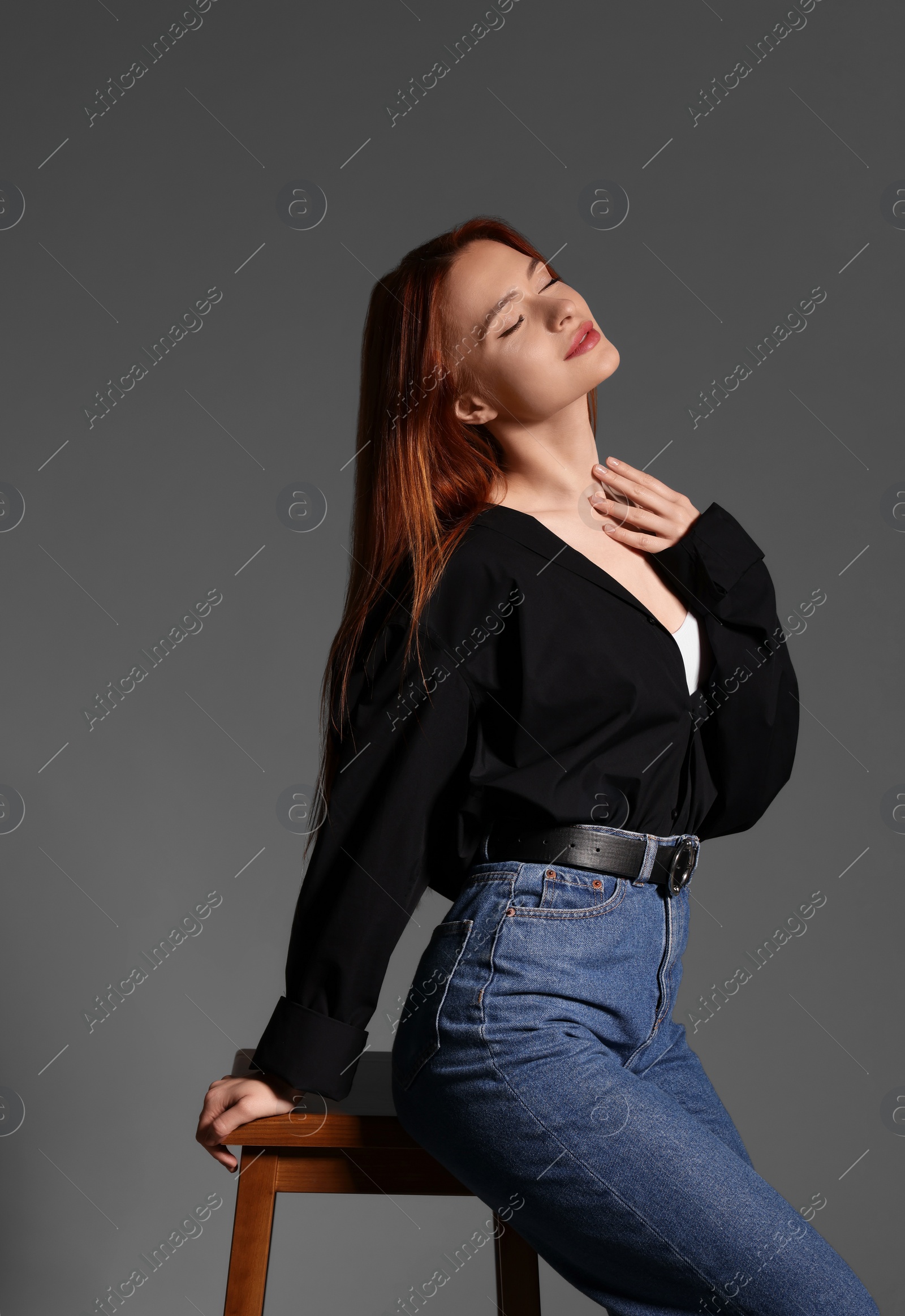 Photo of Beautiful young woman sitting on stool against gray background