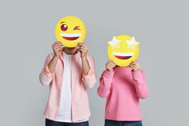 People covering faces with happy emoticons on grey background