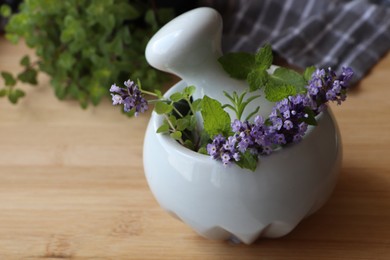 Mortar with fresh lavender flowers, herbs and pestle on wooden table, closeup