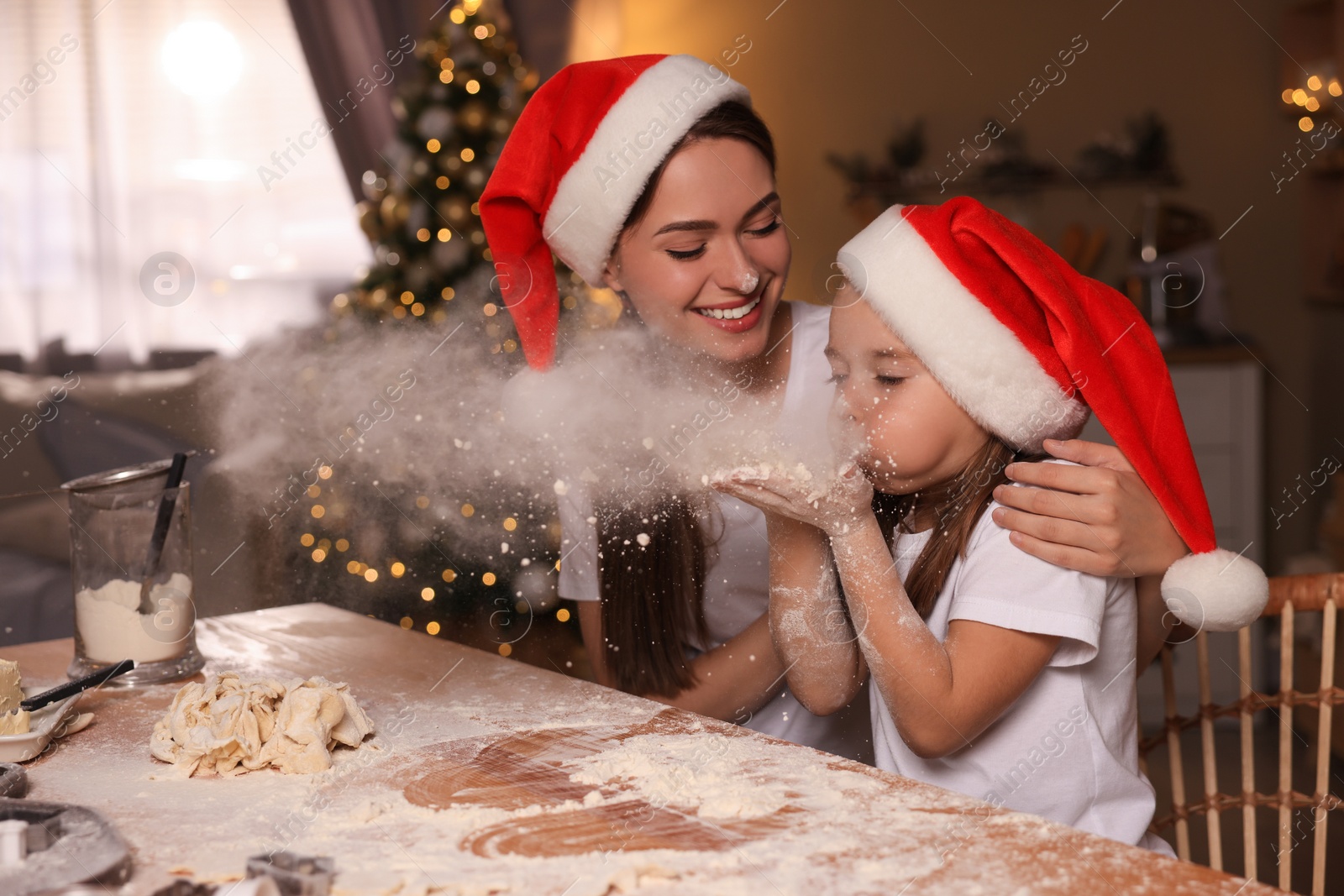 Photo of Mother with her cute little daughter having fun while making dough for Christmas cookies in kitchen