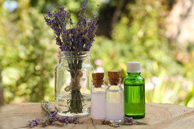 Photo of Beautiful lavender flowers and bottles of essential oil on wooden stump
