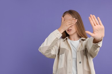 Embarrassed woman covering face with hand on violet background, space for text