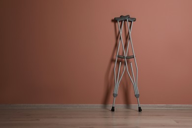 Photo of Pair of axillary crutches near pale pink wall. Space for text