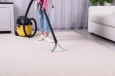 Photo of Woman cleaning carpet with vacuum cleaner, closeup