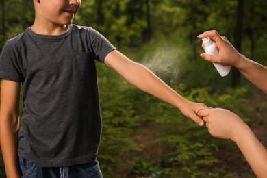 Photo of Woman applying insect repellent on her son's arm in park, closeup. Tick bites prevention