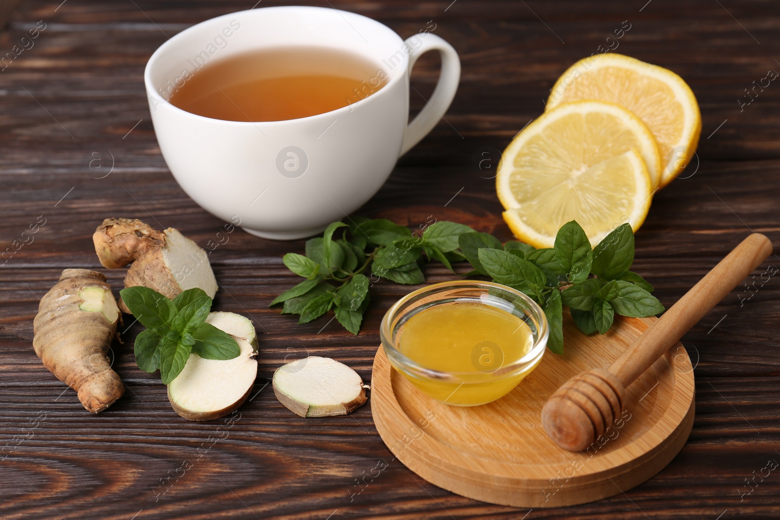 Photo of Bowl with honey for tea, lemon, mint and ginger on wooden table