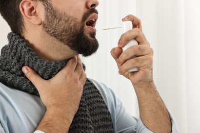 Photo of Young man with scarf using throat spray indoors, closeup