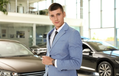 Young salesman near new car in modern dealership