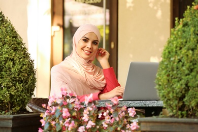 Muslim woman using laptop in outdoor cafe