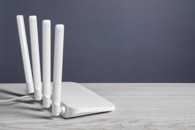 Photo of New stylish Wi-Fi router on white wooden table. Space for text