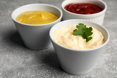 Photo of Bowls with mustard, ketchup and mayonnaise on light grey table, closeup