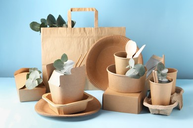 Photo of Eco friendly food packaging. Paper containers, tableware, bag and eucalyptus branches on white table against light blue background