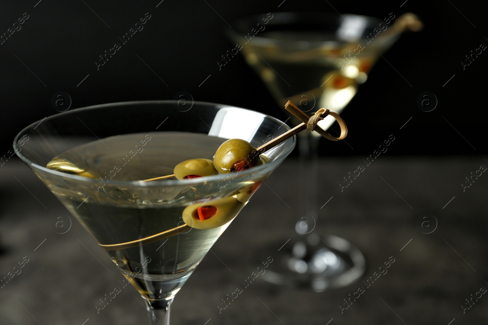 Photo of Glasses of Classic Dry Martini with olives on grey table against black background, closeup