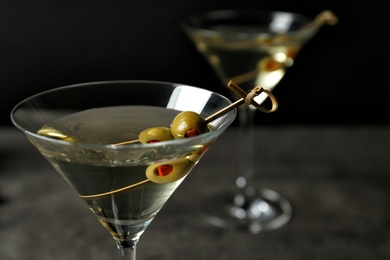 Photo of Glasses of Classic Dry Martini with olives on grey table against black background, closeup