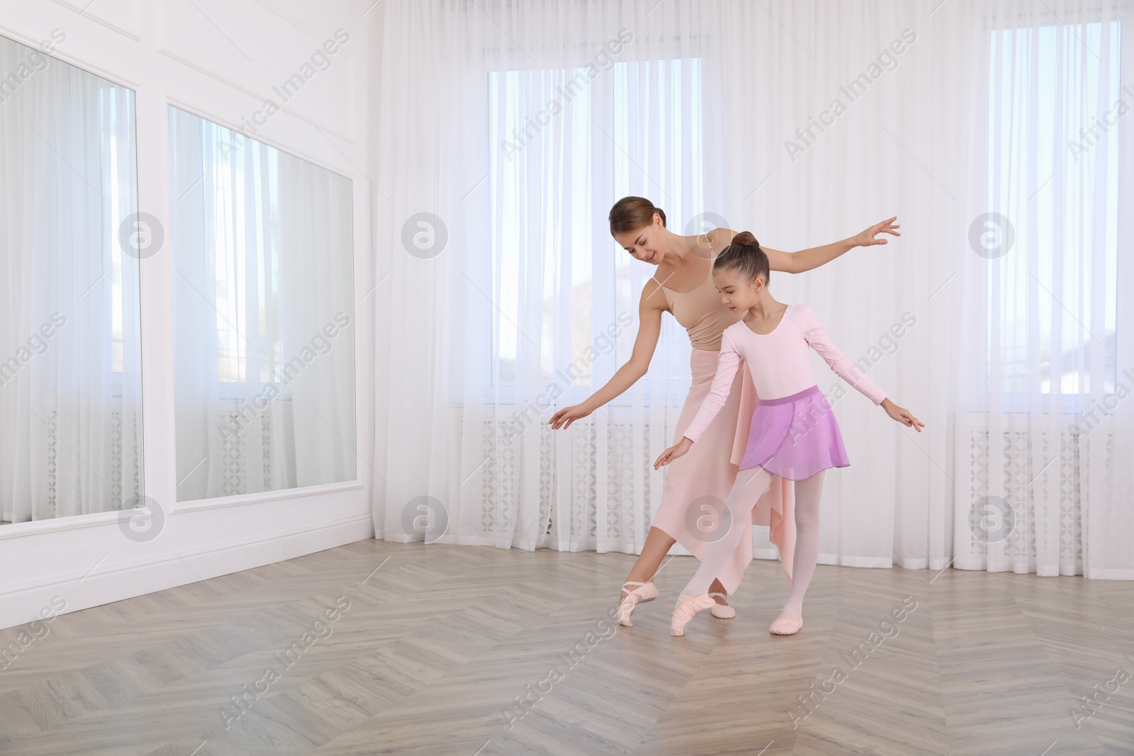 Photo of Little ballerina and her teacher practicing dance moves in studio. Space for text 