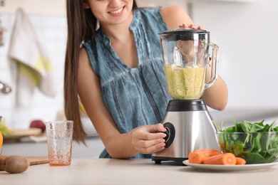 Young woman preparing tasty healthy smoothie at table in kitchen