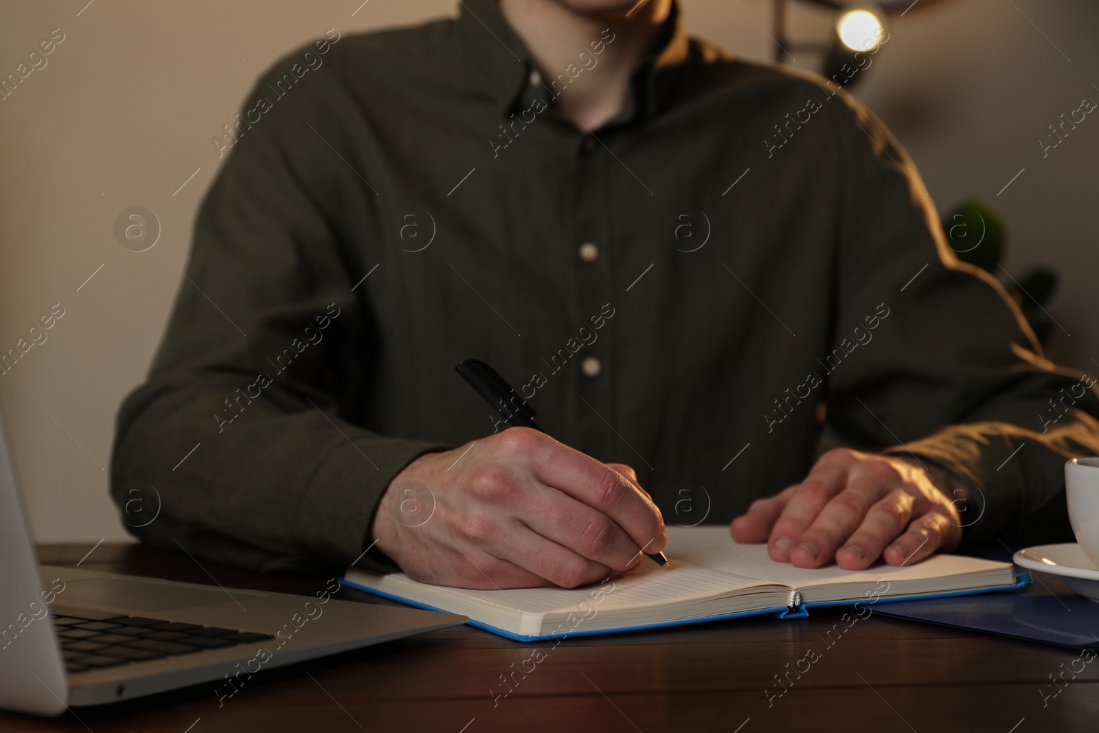 Photo of Man taking notes at wooden table indoors, closeup