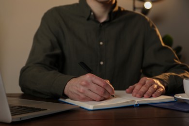 Man taking notes at wooden table indoors, closeup