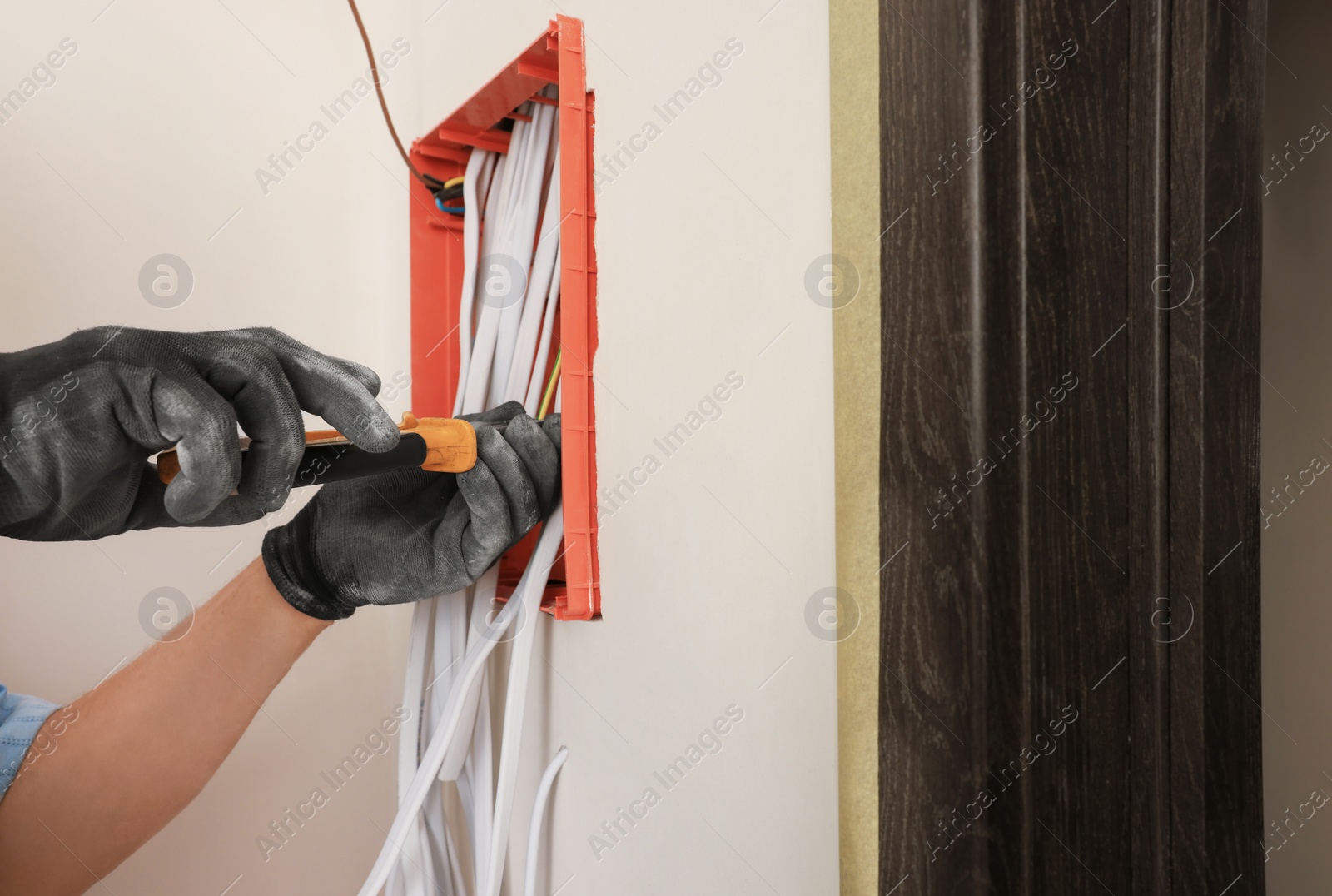 Photo of Electrician with pliers installing switchboard indoors, closeup