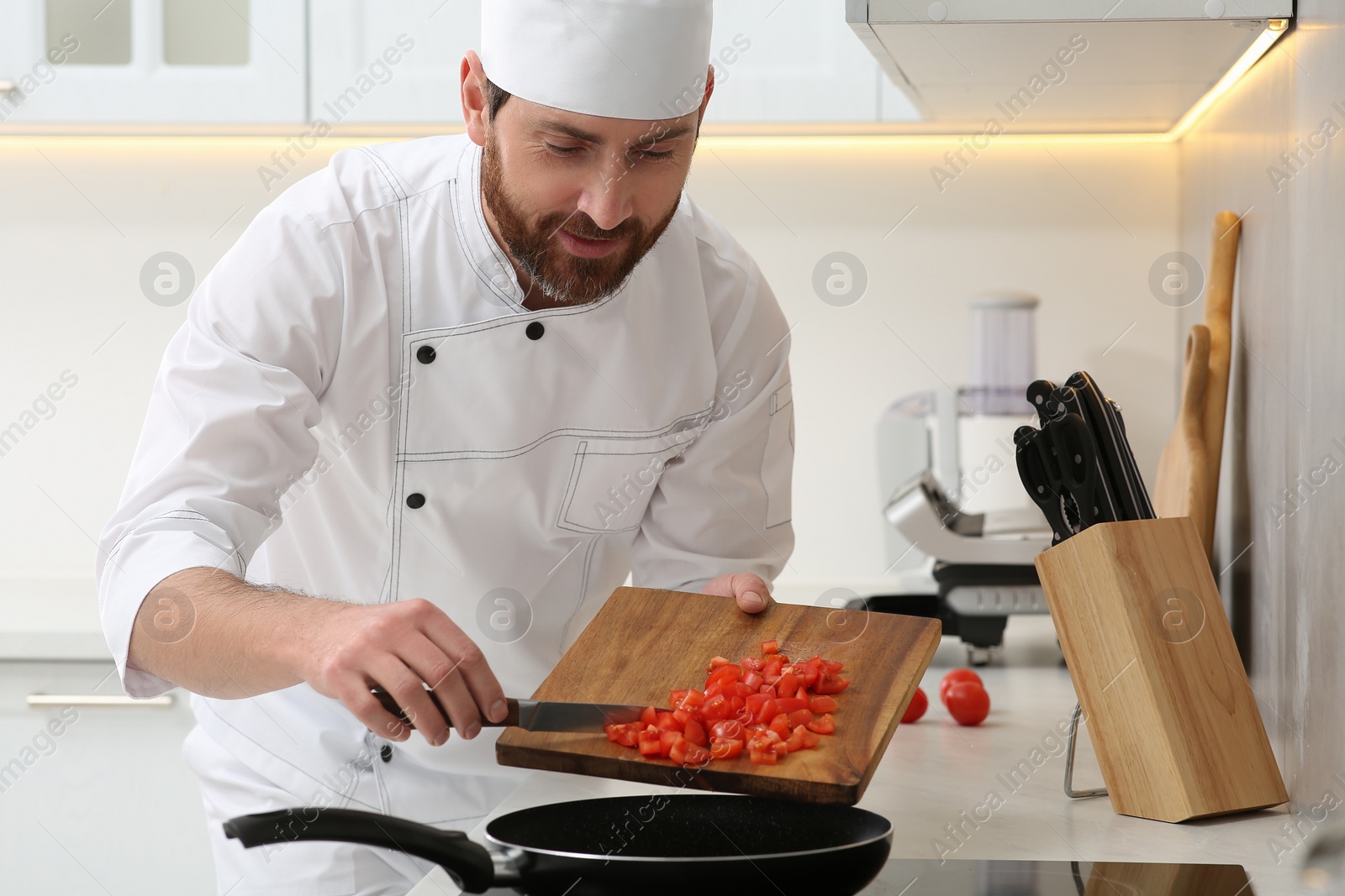 Photo of Professional chef putting cut tomatoes into frying pan in kitchen