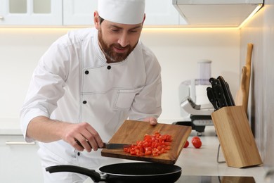 Photo of Professional chef putting cut tomatoes into frying pan in kitchen