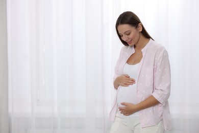 Beautiful pregnant woman near window indoors, space for text