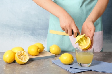 Photo of Woman squeezing lemon juice with reamer into glass on table
