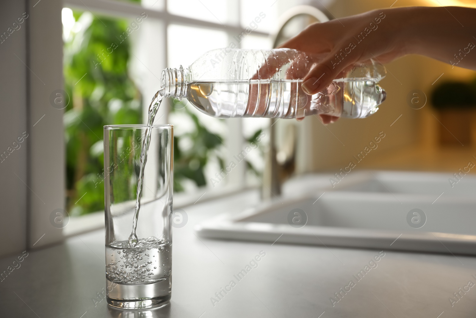 Photo of Woman pouring water from bottle into glass in kitchen, closeup