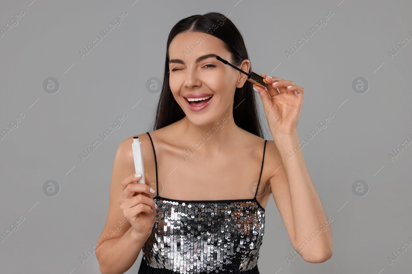 Photo of Beautiful young woman applying mascara on grey background