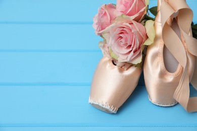 Beautiful beige ballet shoes with cute ribbons and rose flowers on light blue wooden table. Space for text