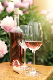 Photo of Glasses and bottle with rose wine on wooden table near beautiful peonies