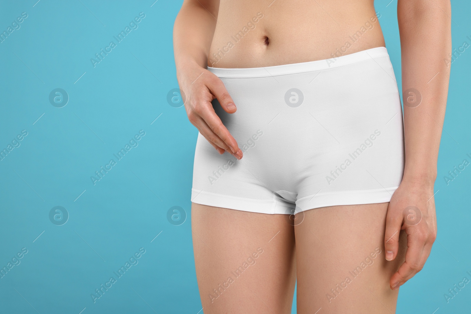 Photo of Woman holding hand near panties on light blue background, space for text. Women's health