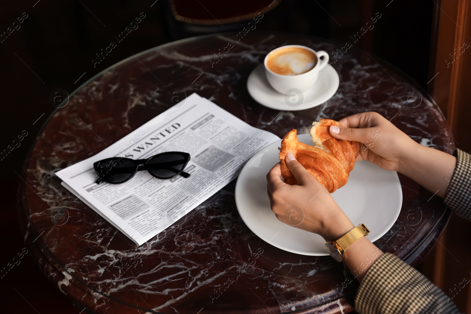 Photo of Woman breaking tasty croissant at black table, closeup