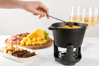 Photo of Woman dipping piece of bread into fondue pot with tasty melted cheese at white wooden table, closeup