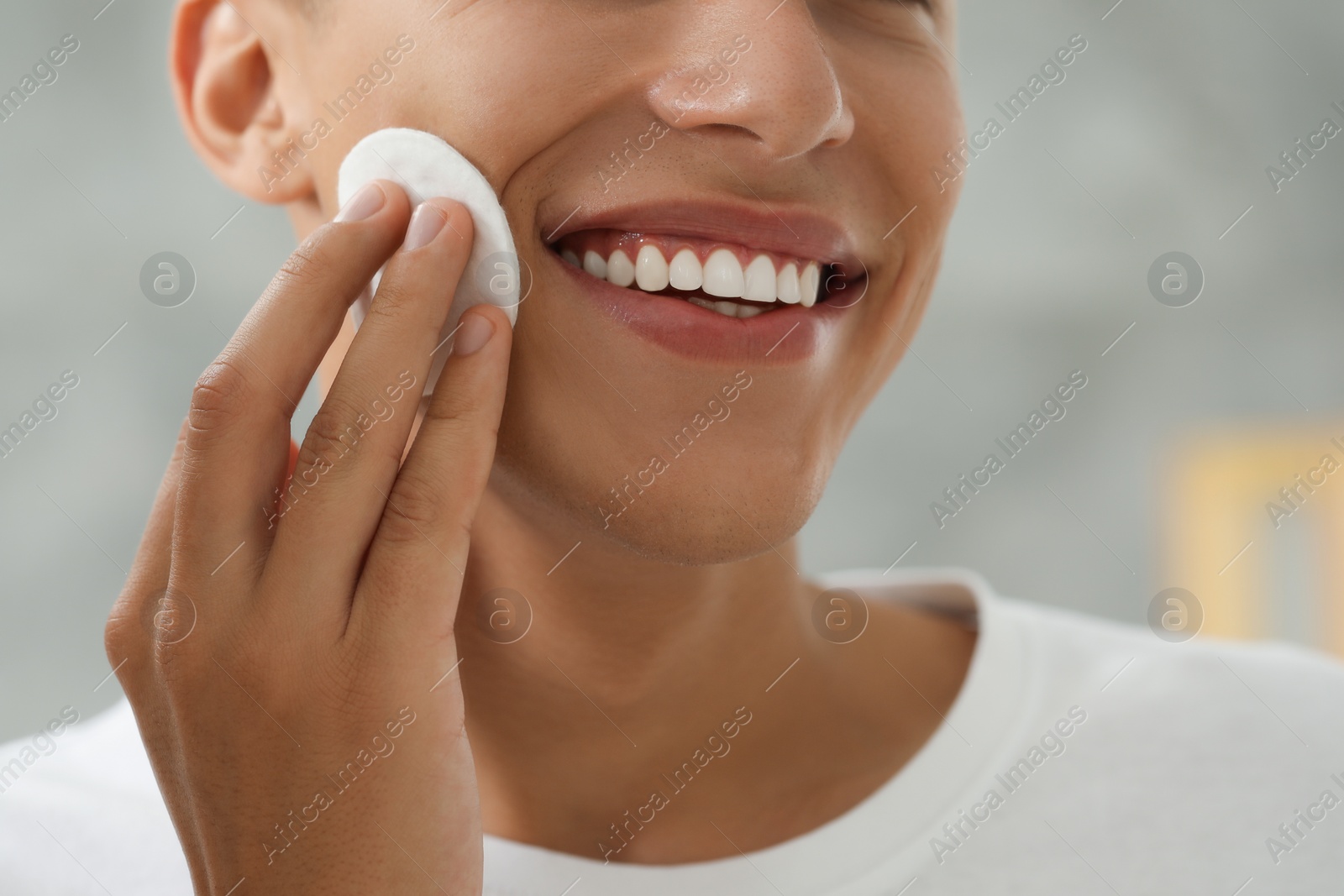 Photo of Man cleaning face with cotton pad against blurred background, closeup