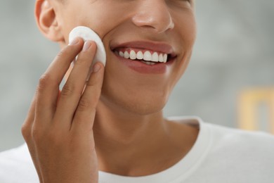 Photo of Man cleaning face with cotton pad against blurred background, closeup