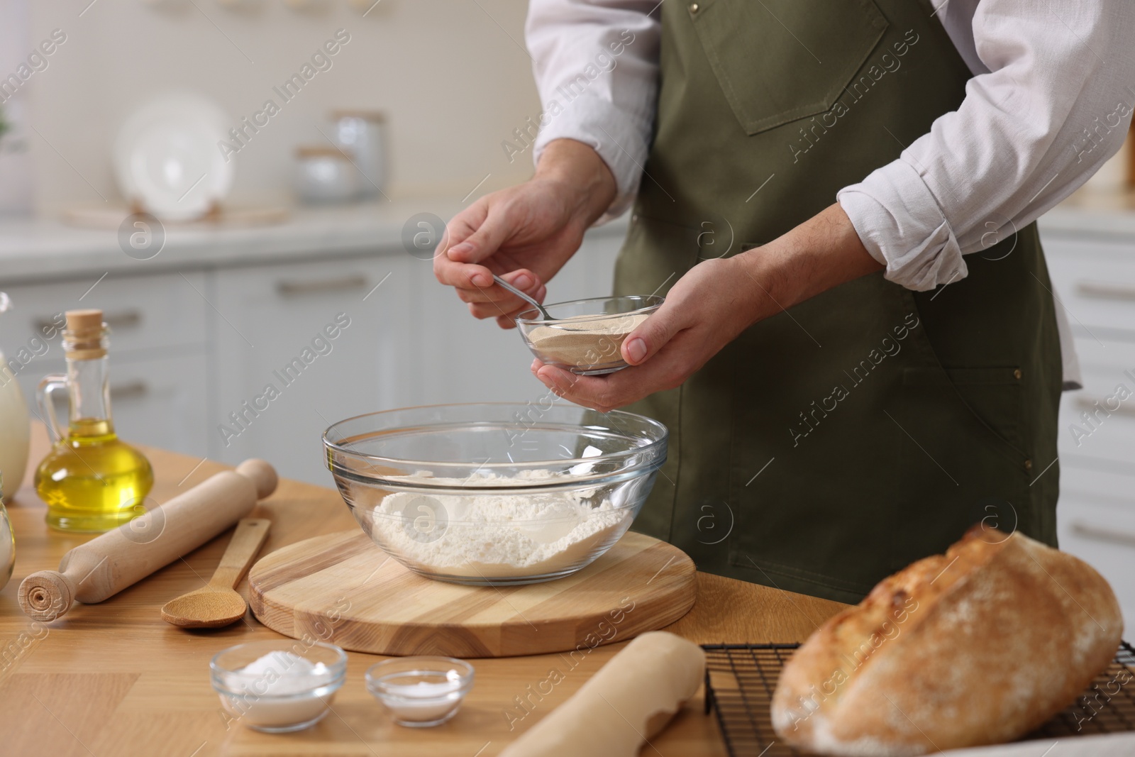 Photo of Making bread. Man putting dry yeast into bowl with flour at wooden table in kitchen, closeup