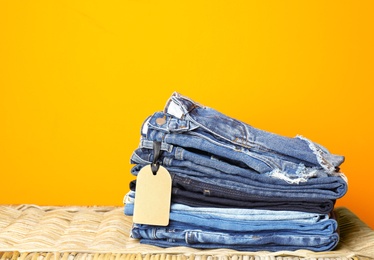 Photo of Stack of jeans on wicker chest against color background