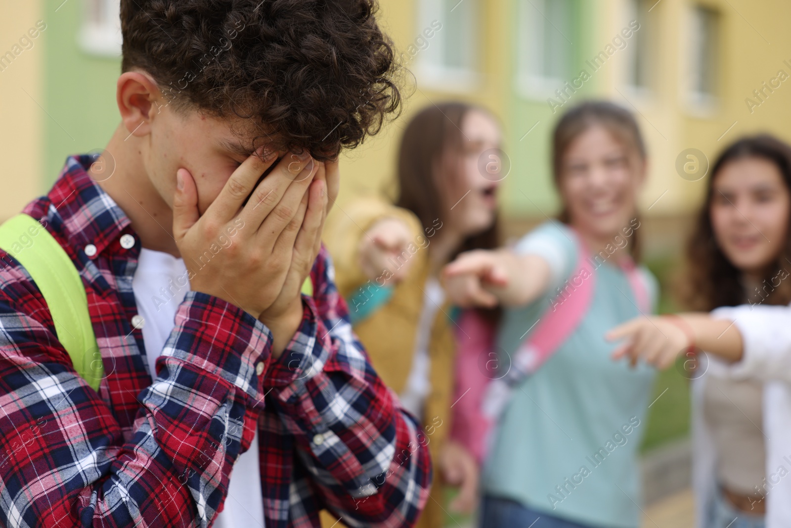 Photo of Teen problems. Group of students pointing at upset boy outdoors, selective focus