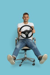 Photo of Happy man on chair with steering wheel against light blue background
